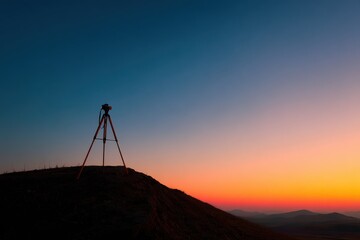 Silhouette of a surveyor tripod standing on a hill at sunrise. Engineering measurement background.