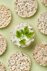 Puffed rice cakes with cream cheese and parsley on a green background. Top view