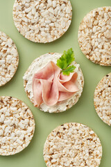 Puffed rice cakes with cream cheese and ham on a green background. Top view