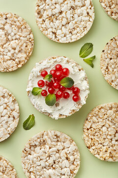 Puffed rice cakes with cream cheese and red currant topped with mint leaves on a green background. Top view