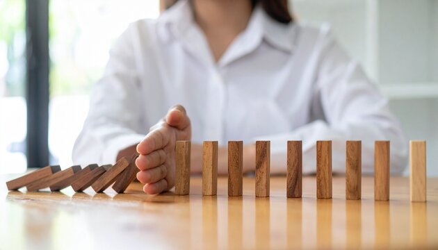 Hand Stopping Domino Effect for Risk Management and Crisis Prevention Concept a businessman's hand intervening to stop a falling row of wooden dominoes, symbolizing risk management, crisis interventio