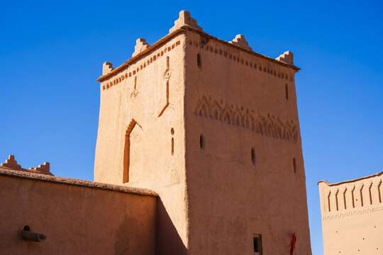 Traditional adobe tower with intricate designs under a clear blue sky. Ouarzazate, Morocco