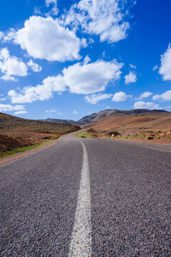 Empty winding road through rocky landscape under a clear blue sky with scattered clouds. Ouarzazate, Morocco