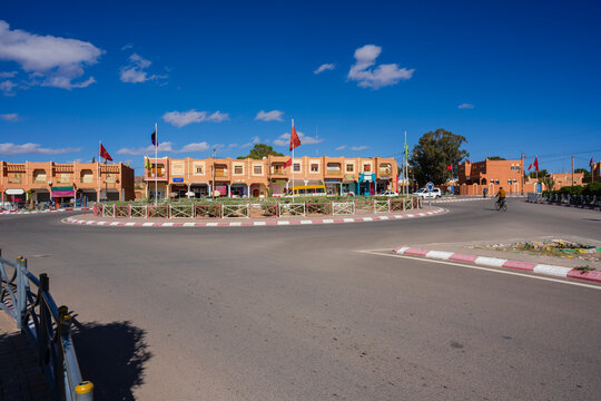 Circular town square with red-orange buildings under a vivid blue sky, flags fly on buildings. Ouarzazate, Morocco