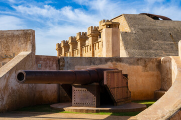 An old cannon sits in a historic fort with stone walls under a partly cloudy blue sky. Rabat, Morocco