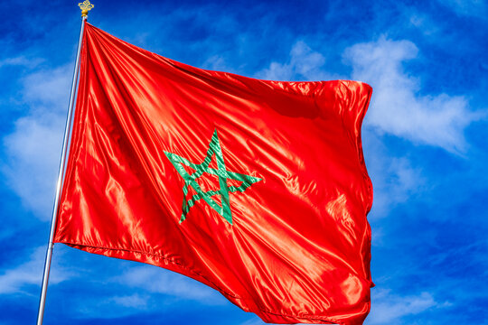 A vibrant red flag with a green star flutters against a bright blue sky with scattered clouds. Rabat, Morocco