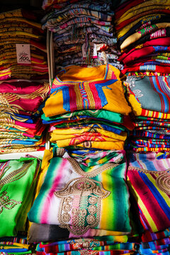 Colorful stacks of vibrant embroidered fabric and traditional garments in a market setting. Rabat, Morocco