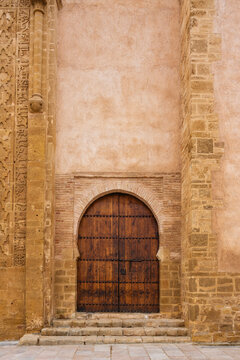 Ornate wooden arched door set in an intricately carved stone wall with brick accents. Rabat, Morocco