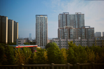 Urban skyline with tall modern buildings and lush green trees below under a clear blue sky. Chengdu, Sichuan, China