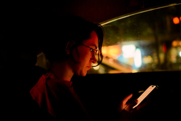 Woman in car using smartphone with city lights reflecting through the window at night. Chengdu, Sichuan, China