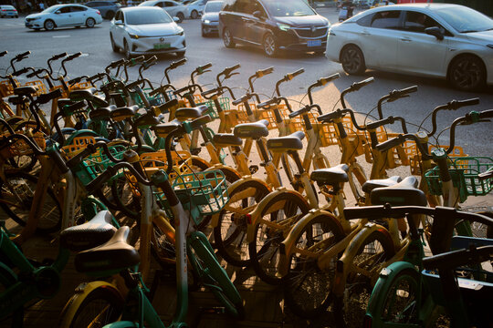 Rows of parked bicycles on a city street with passing cars in the background at sunset. Chengdu, Sichuan, China