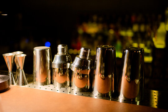 Cocktail shakers and jiggers on a dimly lit bar counter with a blurred background.  Chengdu, Sichuan, China