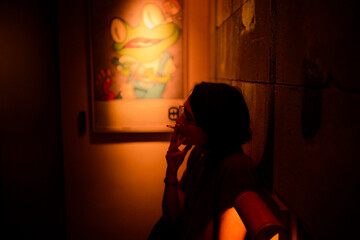 Woman smoking in a dimly lit room with a frog poster on the wall. Chengdu, Sichuan, China