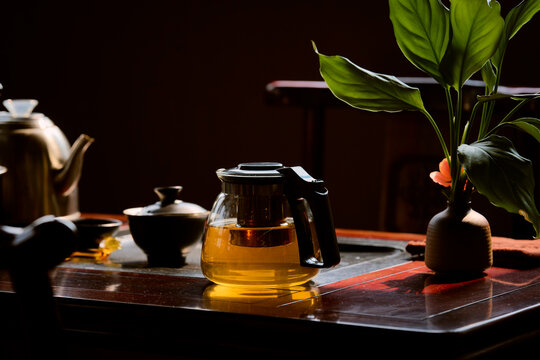 A glass teapot filled with tea on a wooden table beside a potted plant in warm lighting. Li River, Li Jiang, Guangxi, China