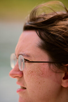 Close-up side profile of a woman wearing glasses with wind-swept hair outdoors. Li River, Li Jiang, Guangxi, China