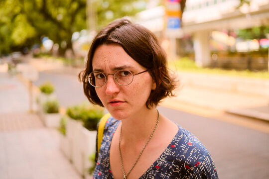 Woman with glasses and short hair looks intently on a sunlit urban street.   Guangzhou, Guangdong, China
