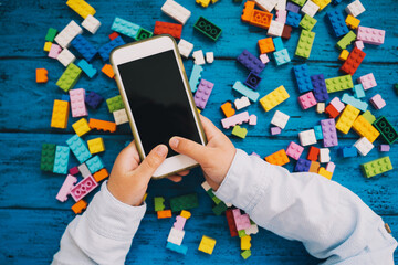 Fototapeta premium Child playing hands with colorful plastic blocks and mobile phone
