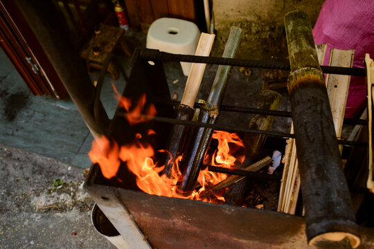 Flaming grill with burning wood and metal pipes in an outdoor setting. Trip from Guilin to Chengdu, Guangxi, Sichuan, China