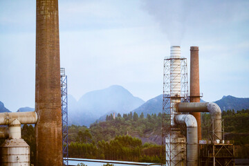 Industrial smokestacks releasing smoke with scenic mountains in the background. Trip from Guilin to Chengdu, Guangxi, Sichuan, China