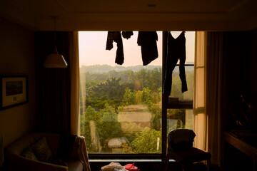 Clothes hang in front of a window with a scenic view of lush green hills. Trip from Guilin to Chengdu, Guangxi, Sichuan, China