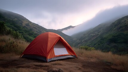 An orange tent is pitched on a grassy hillside overlooking a misty mountain valley at dawn