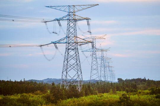 Tall metal pylons stretch across a lush green landscape under a cloudy blue sky. Trip from Guilin to Chengdu, Guangxi, Sichuan, China