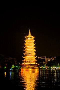 Illuminated pagoda reflecting on the water at night with city lights in the background Trip from Guilin to Chengdu, Guangxi, Sichuan, China