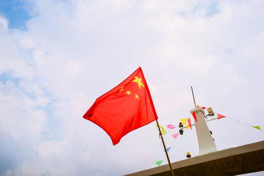 Chinese flag waving atop a boat against a partly cloudy sky. Trip from Guilin to Chengdu, Guangxi, Sichuan, China