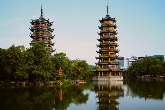 Twin pagodas reflecting in a serene lake surrounded by lush greenery under a clear sky. Trip from Guilin to Chengdu, Guangxi, Sichuan, China