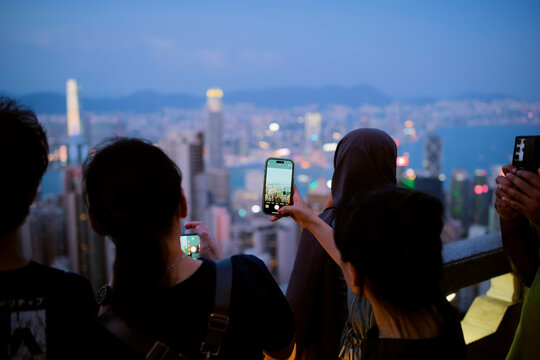 People taking photos of a vibrant city skyline at dusk with smartphones. Hongkong, China