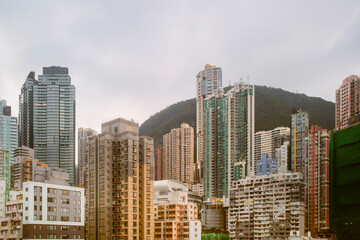Urban cityscape with diverse tall buildings against a mountainous backdrop under cloudy skies. Hongkong, China