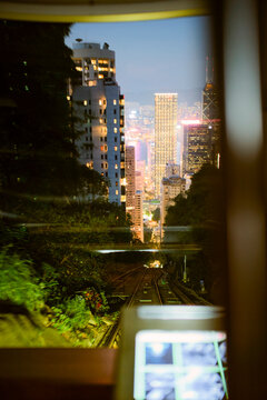City skyline viewed from a funicular railway with lush greenery and illuminated skyscrapers. Hongkong, China
