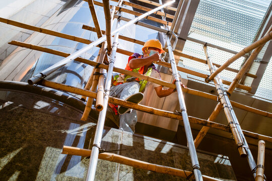 Construction worker climbing bamboo scaffolding on a modern building site. Hongkong, China
