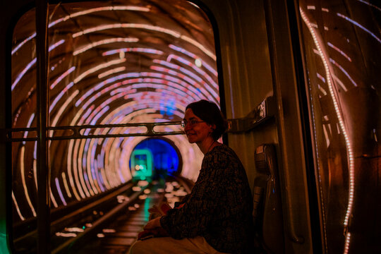 Woman seated inside a tunnel with colorful lights and circular patterns around her. Shanghai, China