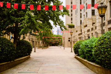 Urban walkway adorned with rows of small red flags, flanked by greenery and tall buildings. Shanghai, China