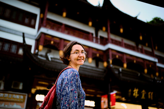Smiling woman with glasses in a blue blouse with patterns stands outside an ornate building. Shanghai, China