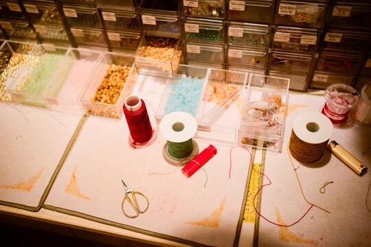 Craft workspace with colorful threads, beads, scissors, and organized storage boxes on a table. Shanghai, China - Powered by Adobe