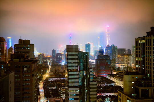 Illuminated city skyline at night with glowing lights and tall skyscrapers against a hazy sky. Shanghai, China