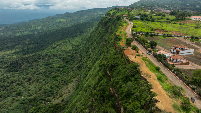 A aerial view of a lush green landscape with a winding road along a steep hillside. Barichara, Colombia