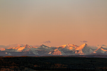 Majestic snow-capped mountains at sunset with a warm glow in a vast open landscape. West of Calgary, Canada