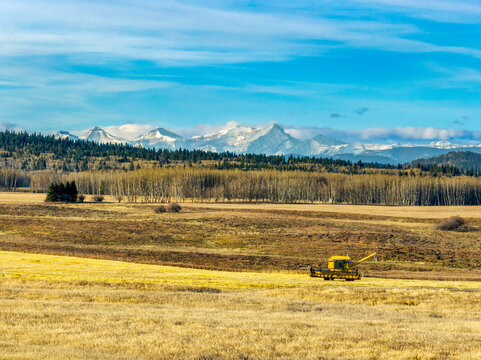 A lone combine harvester in a vast field with distant snow-capped mountains and a blue sky. West of Calgary, Canada