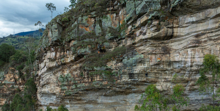 Rock climbers scaling a rugged cliff face with trees and cloudy sky in the background. Colombia