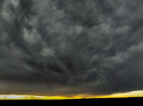Dark storm clouds swirl dramatically above a yellow horizon during sunset. Calgary, Canada