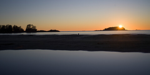 Sunset over a calm ocean with silhouette of trees and islands on the horizon. Tofino, British Columbia, Canada