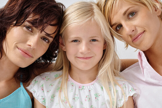 Three women with different hair colors pose closely, smiling gently at the camera. Germany