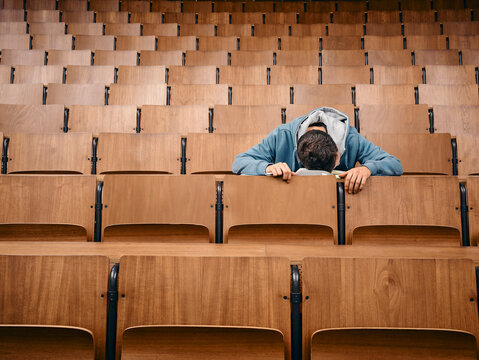 Alone student sleeps on desk in empty lecture hall with wooden seats. Germany