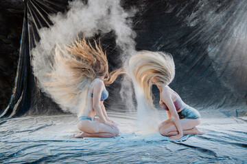 Two women kneel on the floor, tossing powder, creating dynamic hair movement. WA, USA