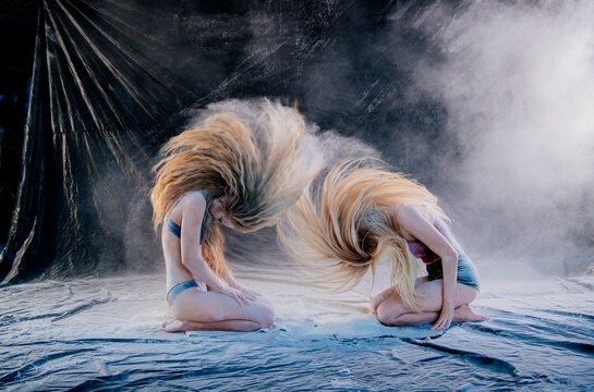 Two women with long hair kneeling on a tarp, flipping hair in a haze of dust and smoke.  WA, USA