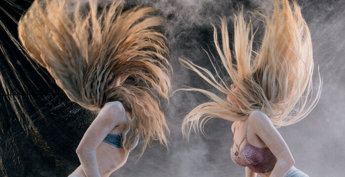 Two women with long hair tossing it in dramatic motion against a smoky backdrop. WA, USA