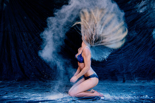 Woman kneeling, flipping hair with flour creating dynamic, artistic motion effect. WA, USA